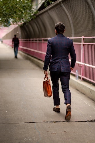 Photo of man walking away while carrying a luxury leather briefcase in brown.