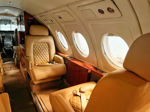 Photo by Yaroslav Muzychenko of the interior of an executive jet with large leather chairs facing each other. Traveling Art Basel Miami.